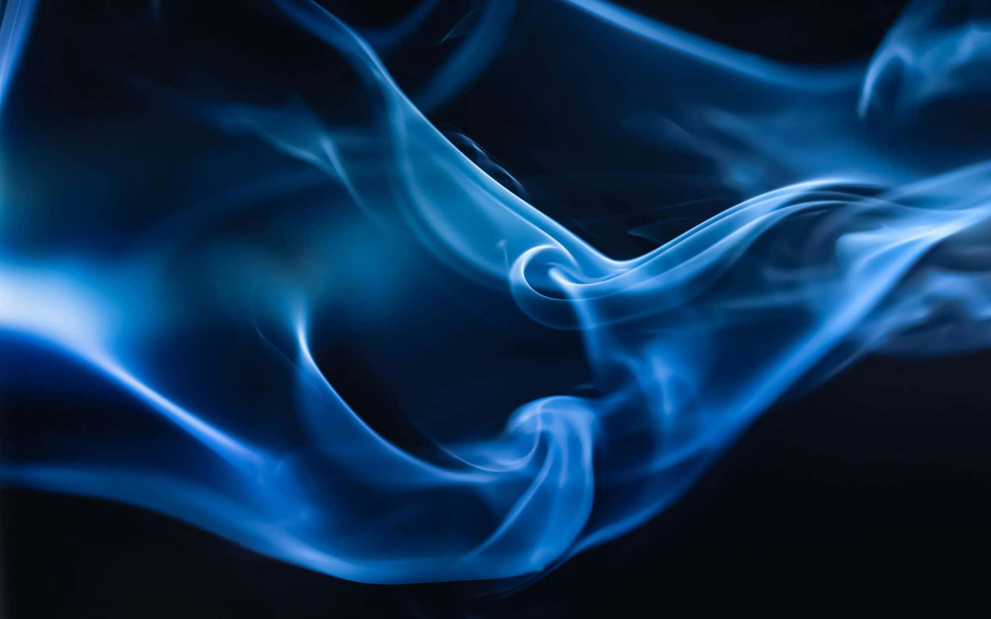 Abstrakte blaue Rauchschwaden bewegen sich sanft auf einem dunklen Hintergrund.