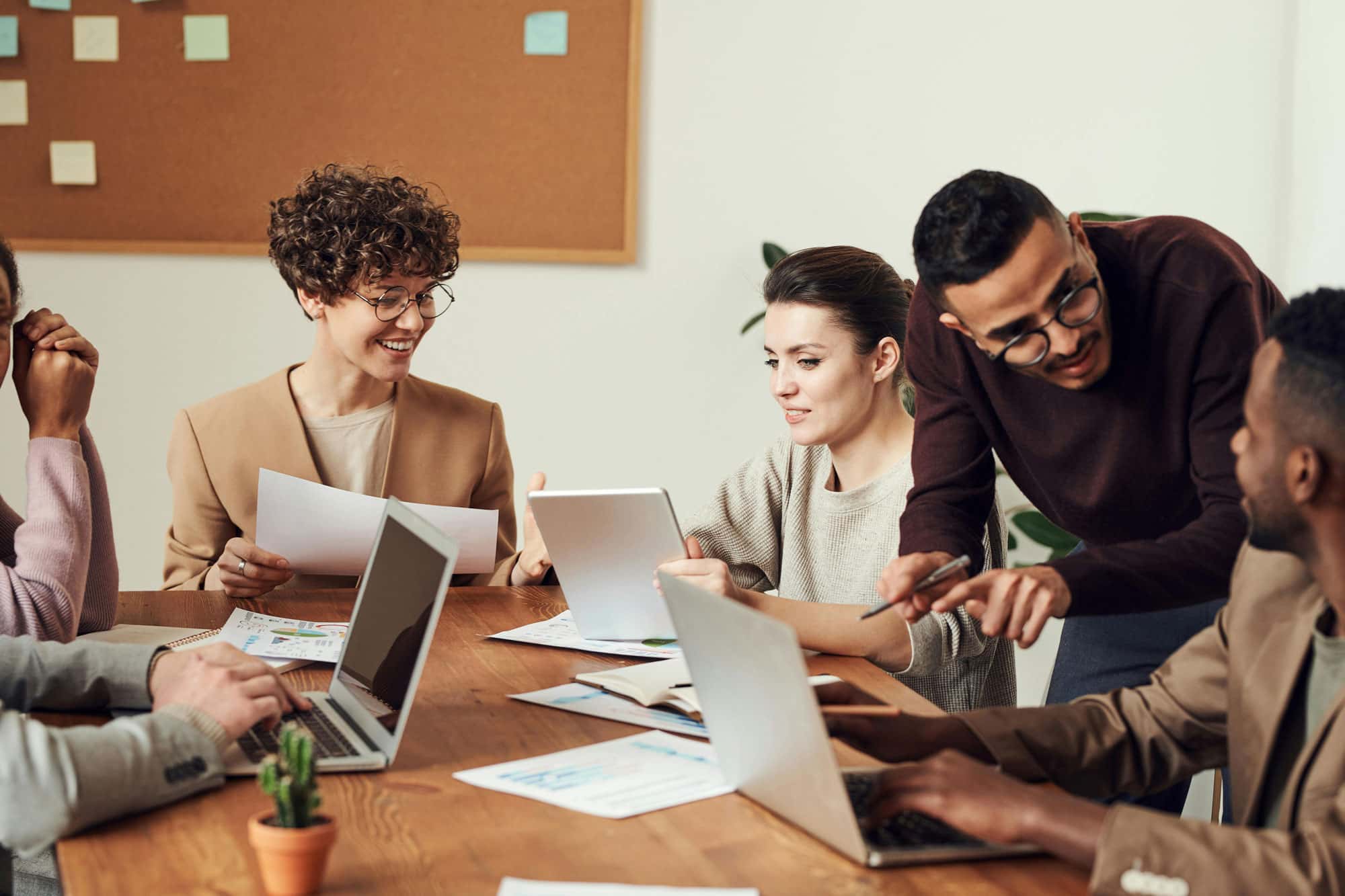 Ein diverses Team von Menschen arbeitet zusammen an einem Tisch, sie besprechen Dokumente und arbeiten an Laptops. Die Atmosphäre ist freundlich und produktiv.