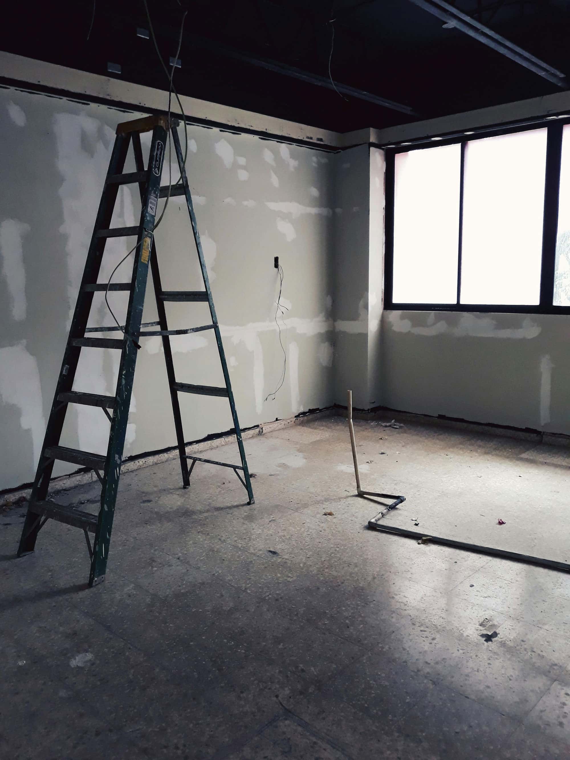 Leere Baustelle mit Leiter und teilweise verspachtelten Wänden in einem Raum mit großem Fenster.