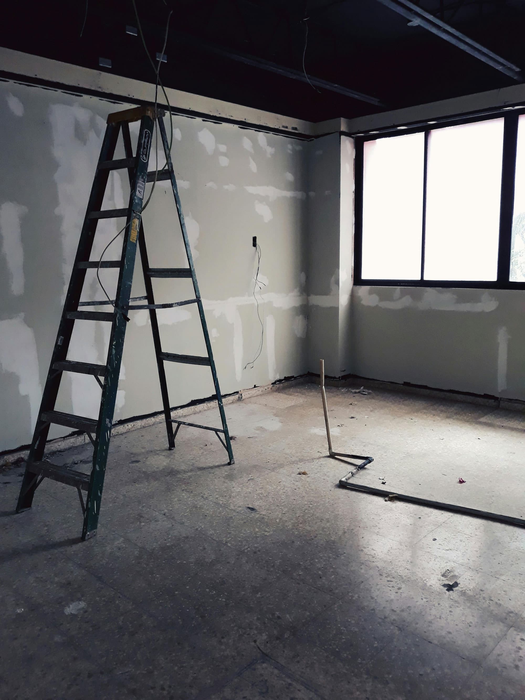 Leere Baustelle mit Leiter und teilweise verspachtelten Wänden in einem Raum mit großem Fenster.